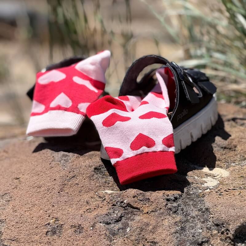Red and white heart-patterned socks on a black sandal against a natural background