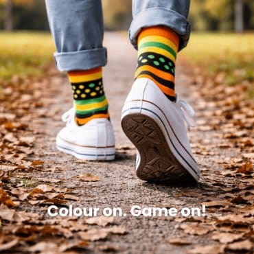 Person wearing colorful socks and white sneakers on a leaf-covered ground.