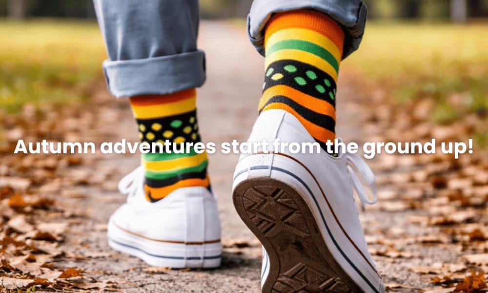 Person wearing colorful socks and white sneakers on a leaf-covered ground with text 'Autumn adventures start from the ground up!'