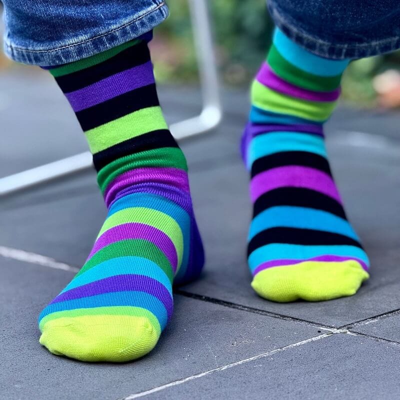 Colorful striped socks worn with blue jeans on a pavement.